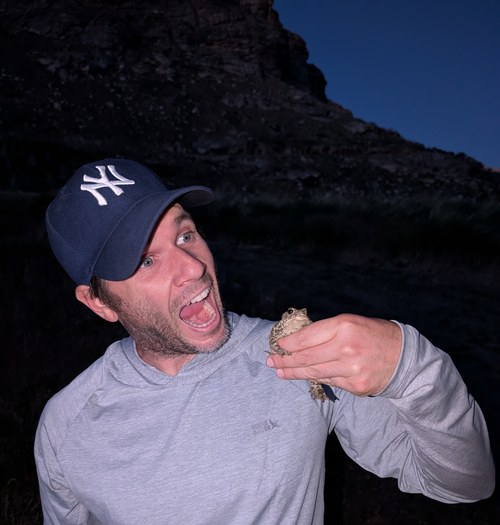 Brett holding up a toad he found on a hike, laughing